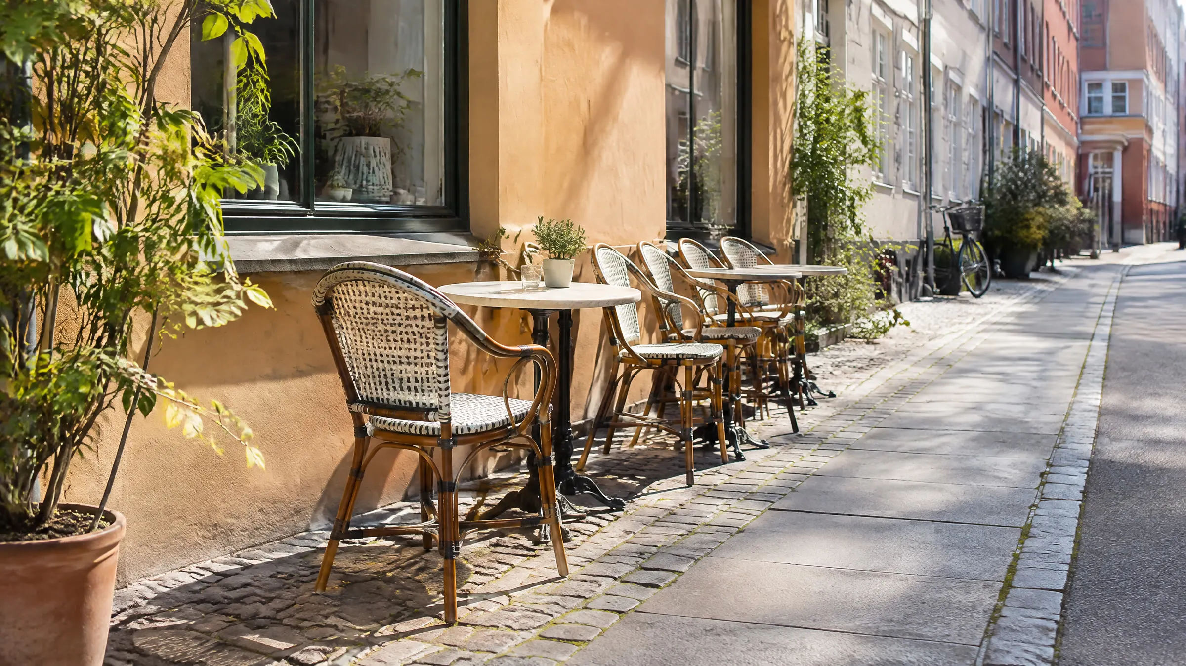 Tomme cafestole og små marmorborde langs et solbeskinnet fortov i en sidegade i København