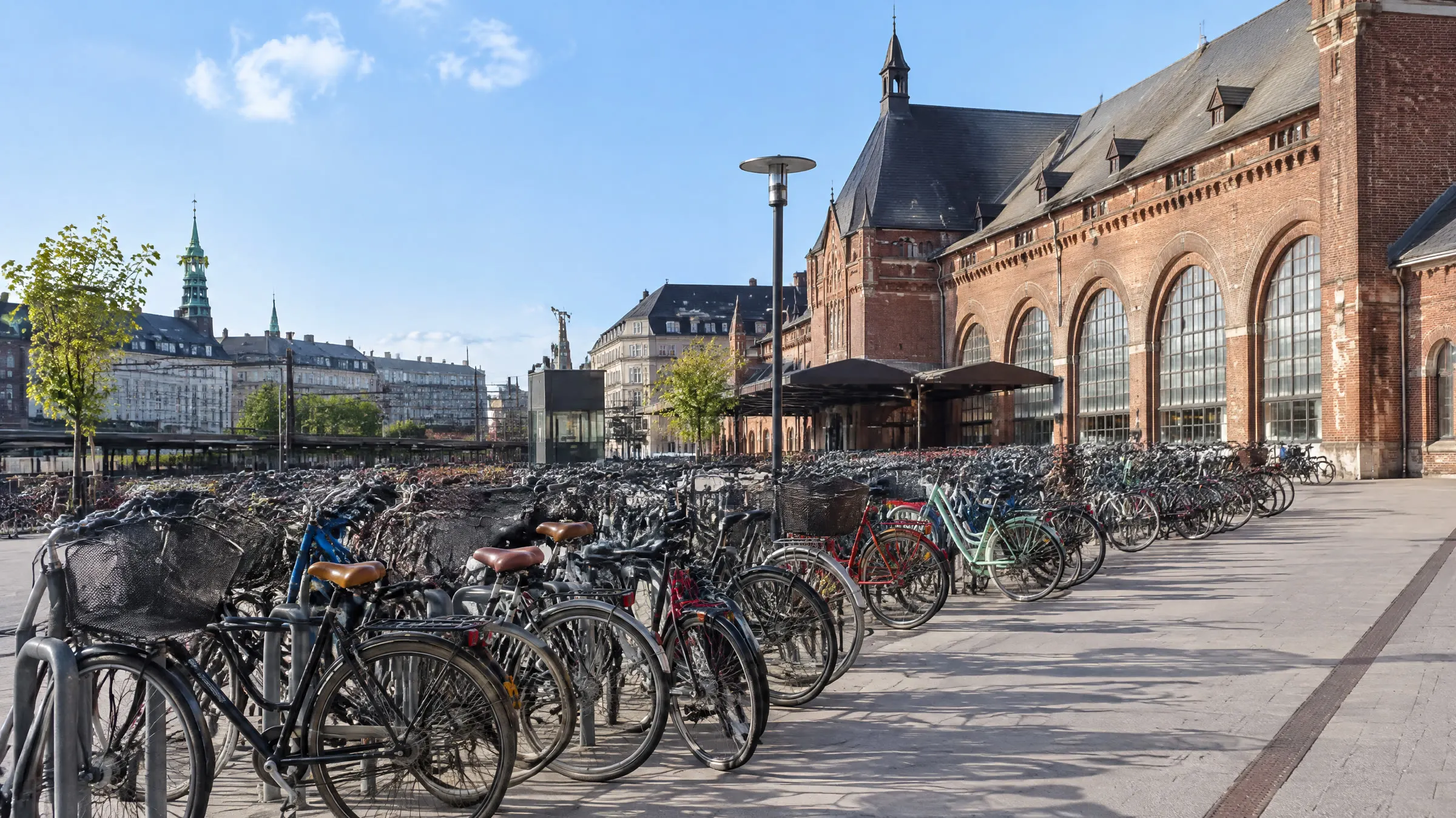 Rækker af parkerede cykler foran en banegård i København i dagslys