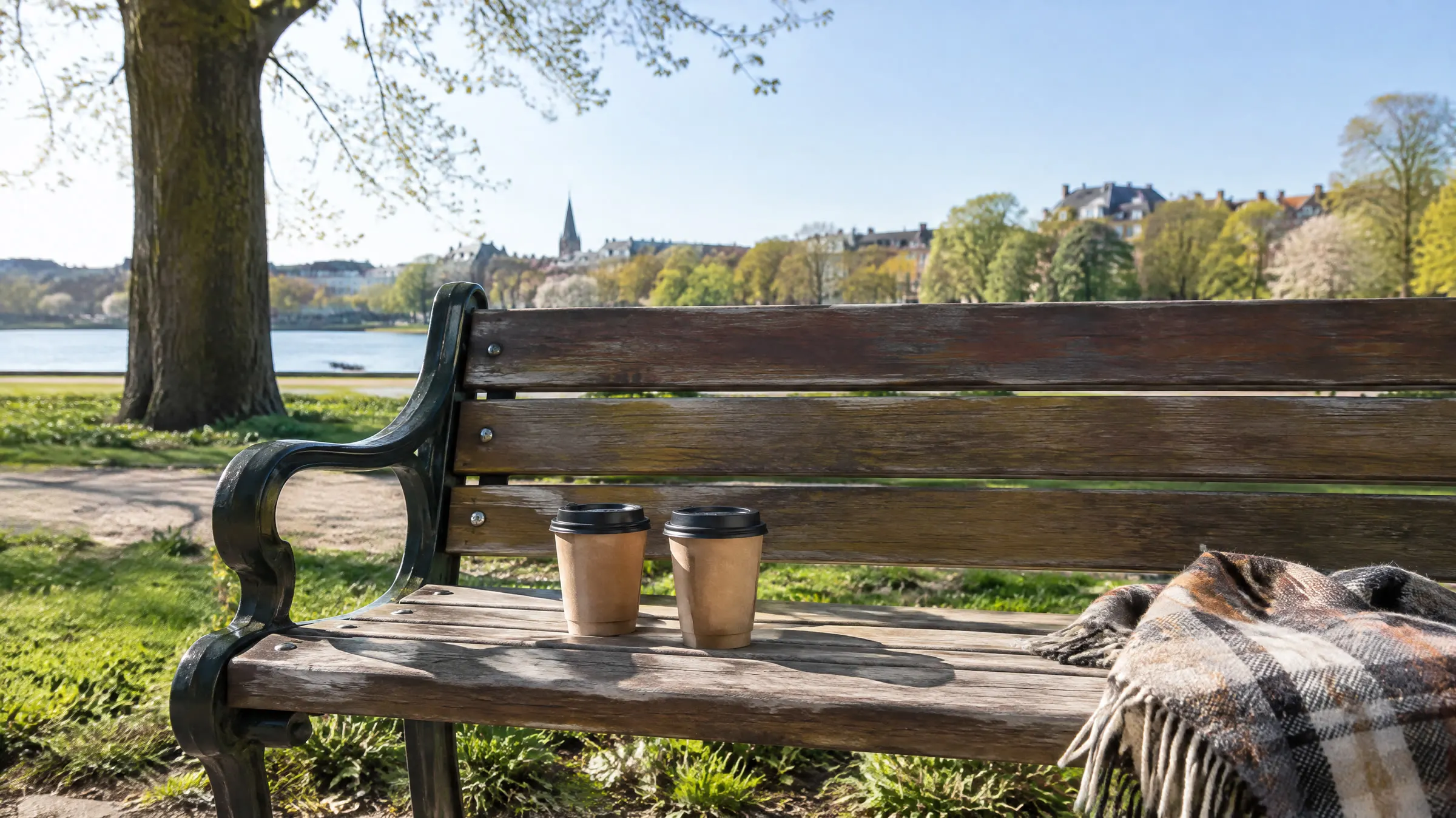 To papkrus med låg og et ternet plaid på en parkbænk ved en sø i forårssol