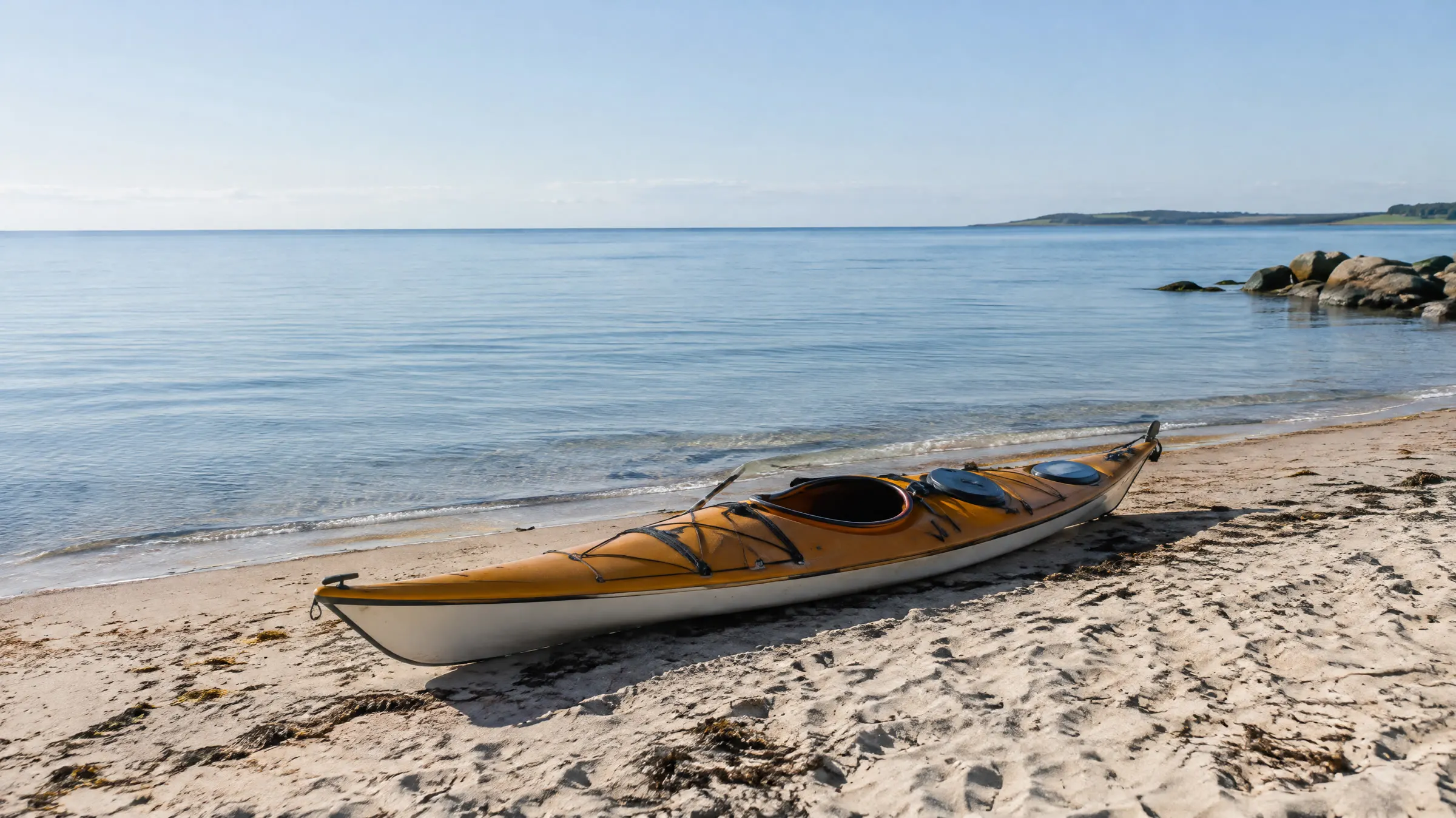 En enkelt kajak trukket op på en dansk sandstrand ved stille hav en morgen
