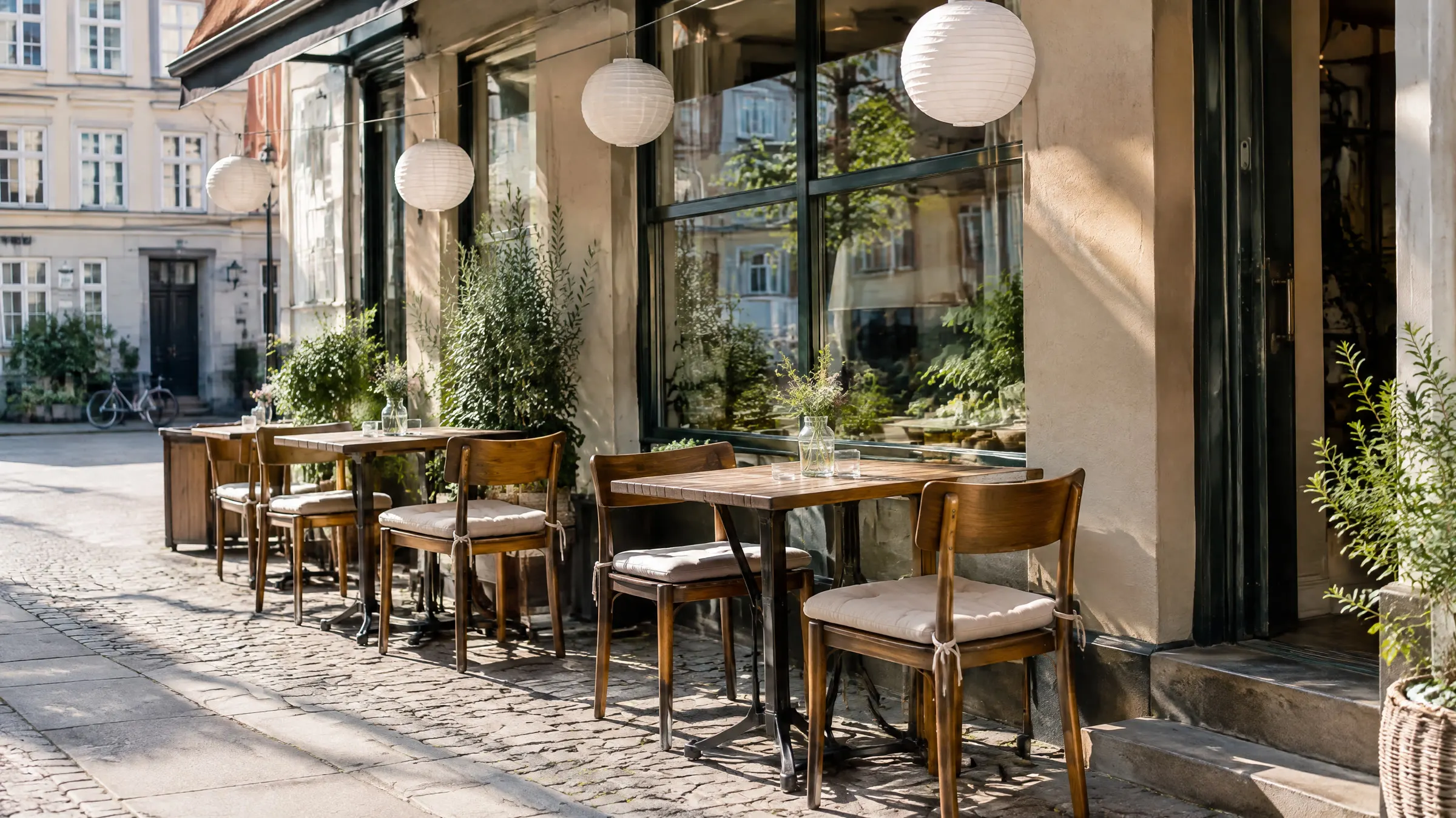 Tomme udendørs borde ved en lille restaurant på en gade i København med papirlamper